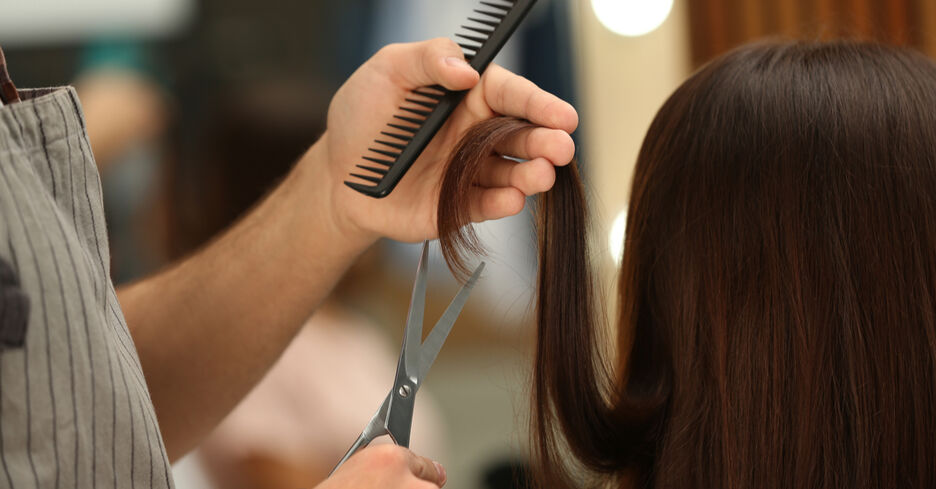 Man sieht wie ein:e Friseur:in lange dunkle Haare schneidet.