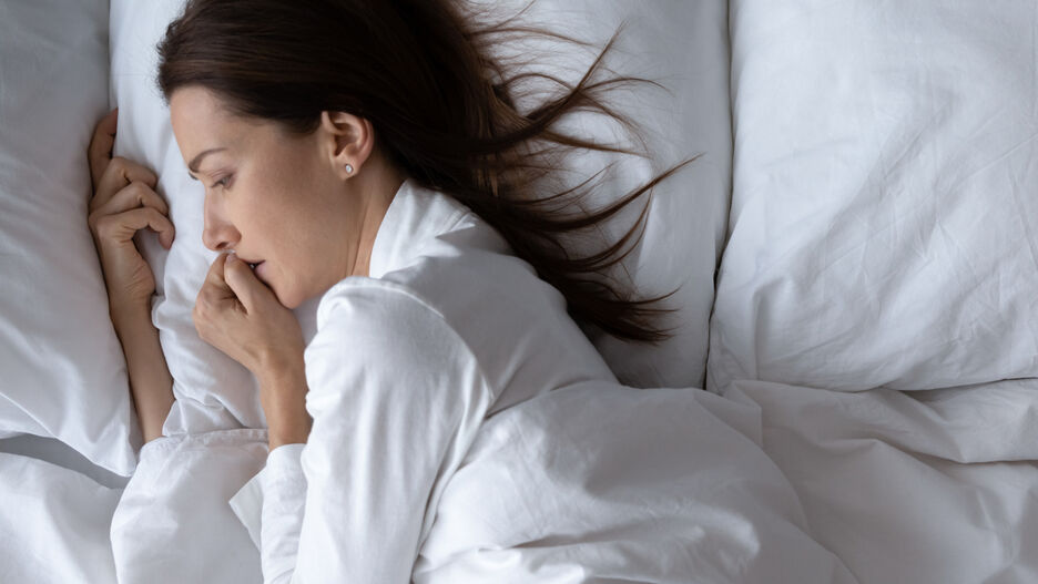 Eine junge Frau liegt ängstlich oder nachdenklich in ihrem Bett.