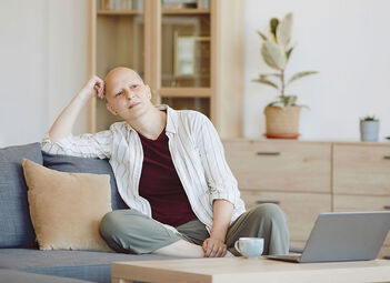 Person mit Glatze sitzt auf der Couch und schaut in die Ferne.