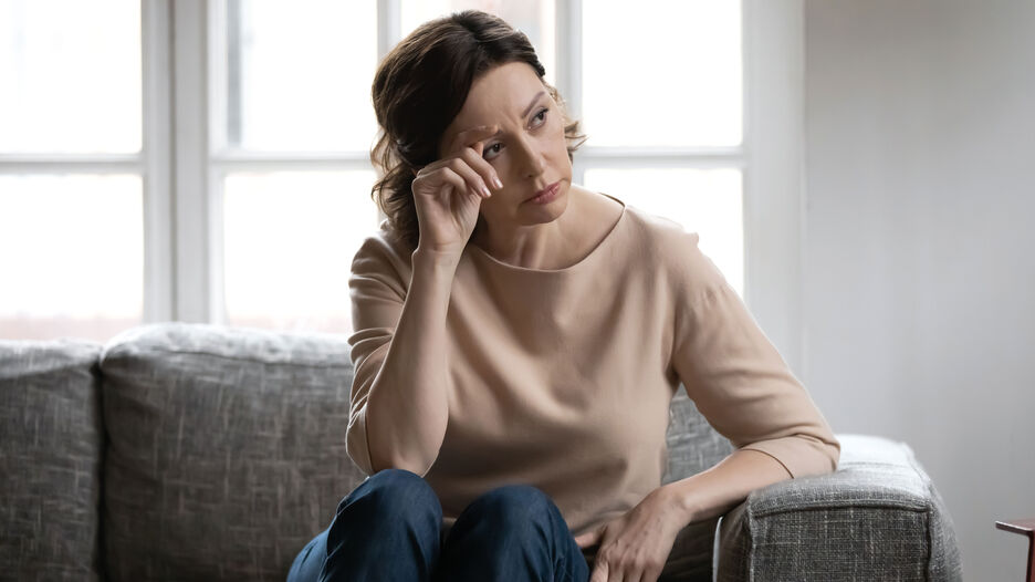 Frau sitzt auf dem Sofa, stützt ihr Gesicht auf die Hand und schaut nachdenklich.