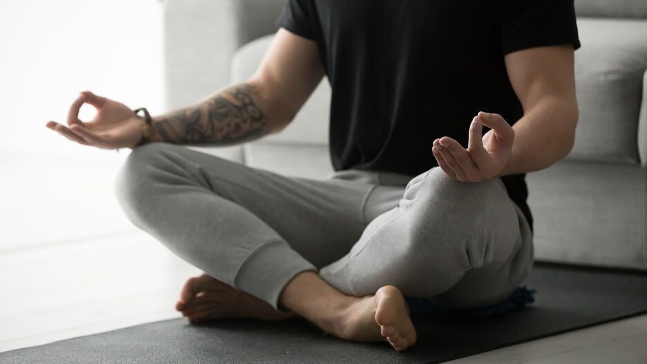 Ein junger Mann sitzt im Schneidersitz auf einer Yoga-Matte.