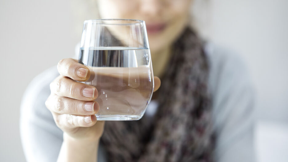 Eine Frau hält ein Glas Wasser in die Kamera.