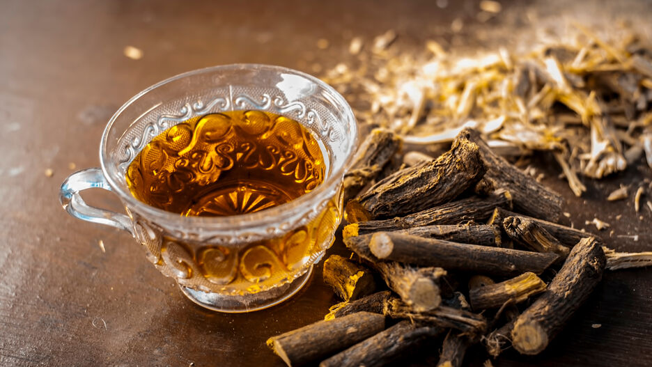 Eine Tasse Süßwurzeltee steht auf einem Tisch. Daneben liegen einige Wurzeln von Süßholz.