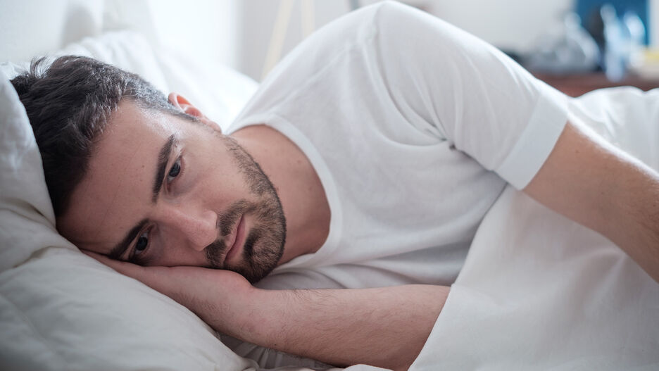 Ein junger Mann liegt schlaflos und nachdenklich im Bett.